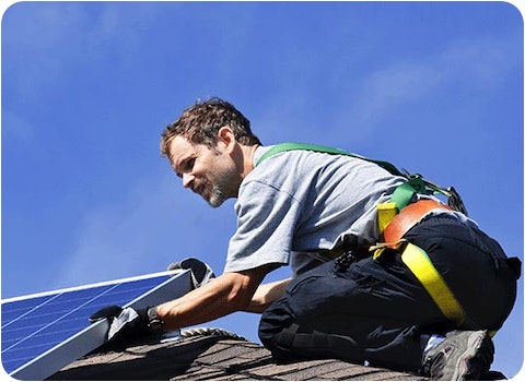 solar installer in harness mounting solar panel on tiled roof